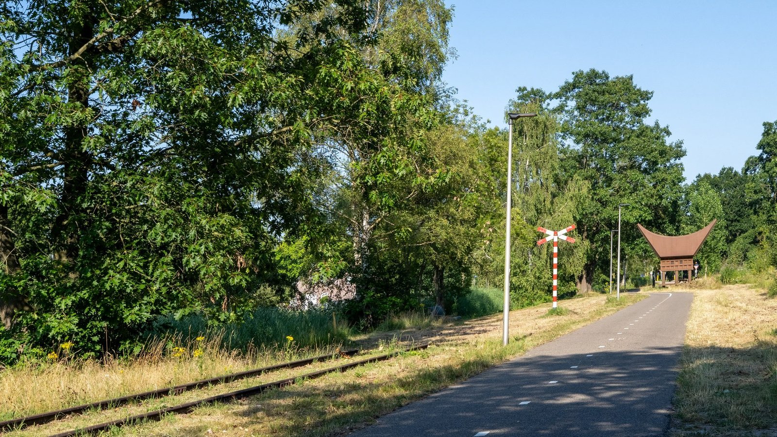 Het oude spoortracé nu, met rails in het gras, een andreaskruis en het kunstwerk Het Koffijhuis.